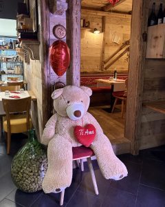 Nella fotografia si vede l'interno di A21 Ristopizza addobbato per San Valentino. In particolare si vede un grosso orso di peluche con un cuore rosso, posizionato su una sedia.
