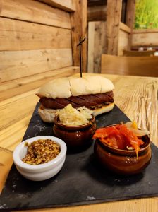 Hot dog con bratwurst accompagnato da senape in grani e peperoni e appoggiato su un tavolo in legno